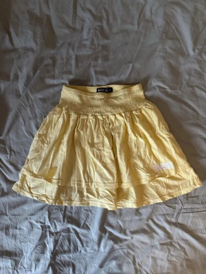 Gul kortkjol från Svea - Söt gul kortkjol från Svea med bred resår i midjan och broderad logga i vitt nedtill. 