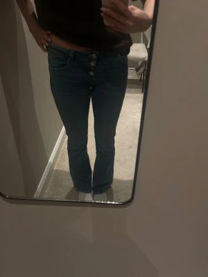 Blå bootcut jeans med knappar - Säljer ett par blå bootcut jeans med hög midja och synliga silverfärgade knappar framtill. Jeansen har klassiska fem fickor och är tillverkade i ett stretchigt denimtyg som sitter snyggt på benen. Perfekta för en avslappnad och trendig look. Byxorna är i stoleken 152 och är från Gina Tricot. Skriv såklart till mig ifall du har några frågor eller funderingar!!❤️
