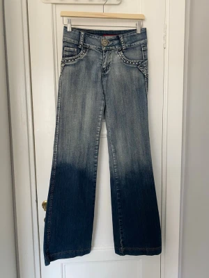 Blå bootcut jeans med nitar 2000s low waist sequins - Säljer ett par riktigt snygga och unika jeans som tyvärr har blivit för små. De har låg midja och utsvängda ben samt coola detaljer av stenar/paljetter. Knappt använda och i mycket bra skick! Alla mått finns på bild i cm 💎💎   