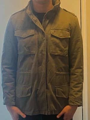 Grön fieldjacket från Tommy Hilfiger - Snygg grön overshirt/field jacket från Tommy Hilfiger med fyra stora fickor framtill och diskret logga på bröstet. Säljer för den sitter lite dåligt på mig. Är 190cm lång. Välkommen vid frågor/fundering
