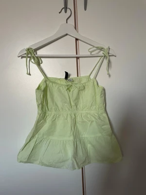 Linnetopp från H&M Divided - Söt  linnetopp från H&M Divided i storlek XS. Toppen har tunna axelband med knyt och volang nedtill för en extra feminin touch. 