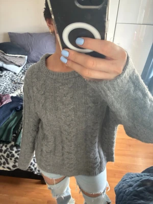 Grå stickad tröja från 157 - Mysig grå stickad tröja från 157 i storlek S. Tröjan har ett klassiskt flätmönster och är långärmad med rund halsringning. Perfekt för kyliga dagar och enkel att matcha med jeans eller kjol.