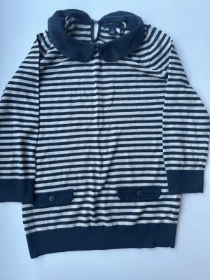 Randig stickad tröja med krage - Säljer en stickad tröja från Polarn O. Pyret med marinblå och vita ränder, stor rund krage och dekorativa fickor med knappar framtill. Tröjan har långa ärmar och ribbade muddar. Perfekt för dig som gillar klassisk och söt stil.