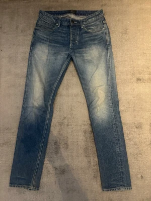 Neuw Stockholm jeans  - Säljer ett par blå slim fit jeans med snygga slitningar och tvättade detaljer på framsidan. Klassisk femficksmodell med normal midja och raka ben. Jeansen har en modern look och passar perfekt till en avslappnad stil.