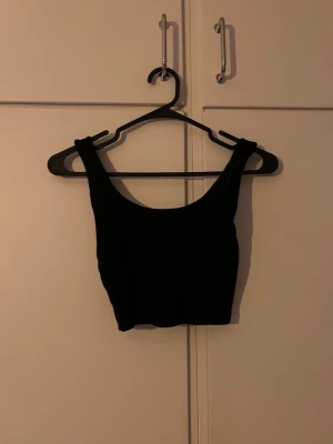 Svart croppad linnetopp - Snygg svart croppad linnetopp med breda axelband och rundad urringning. Perfekt att styla med höga jeans eller kjol för en trendig look. Enkel och stilren design som passar till många outfits.