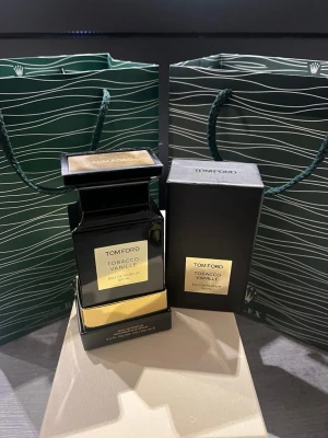 Tom Ford Tobacco Vanille EdP 100ml - Lyxig parfym från Tom Ford, Tobacco Vanille, i en elegant svart glasflaska med guldfärgade detaljer. Flaskan rymmer 100 ml och har en exklusiv, stilren design med matchande svart kartong. Doften är känd för sina varma, kryddiga och söta toner.