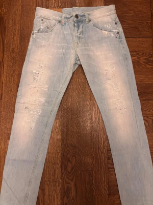 Ljusblå dondup jeans - Säljer ett par ljusblå jeans med snygga slitningar och distressed detaljer på benen. Jeansen har klassisk femficksmodell och raka ben. Perfekta för en avslappnad och trendig stil. Materialet är mjuk denim i bomull. Väldigt fina skräddargjorda slitningar och dem är perfekta till sommaren. Kolla in profilen för liknande par!