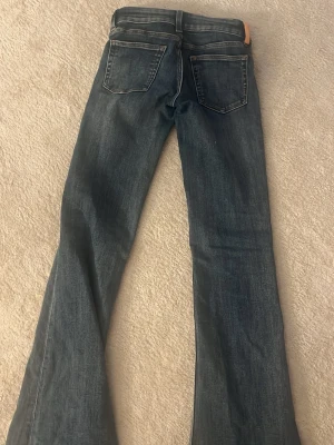 Mörkblå bootcut jeans - Säljer ett par mörkblå bootcut jeans med klassisk femficksdesign och lätt slitna detaljer. Jeansen har en snygg tvätt och vida ben som ger en retrovibe. Perfekta för dig som gillar en avslappnad men trendig look. Jag har tagit bort lappen där back men hoppas det inte gör något 