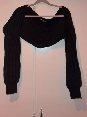 Svart ribbstickad bolero - Trendig svart ribbstickad bolero med långa ärmar och breda muddar. Perfekt att slänga över en topp för en cool lager-på-lager-look. Mjuk och stretchig kvalitet som sitter snyggt på axlarna.