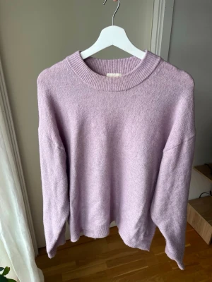 Ljuslila stickad tröja från H&M - Säljer en ljuslila stickad tröja från H&M med rund halsringning och avslappnad passform. Tröjan har ribbade muddar vid hals, ärmslut och nederkant. Perfekt för lager på lager och enkel att styla till olika outfits.