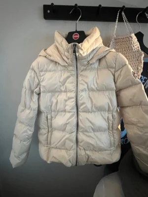 Beige pufferjacka från Colmar - Snygg beige pufferjacka från Colmar med huva och dragkedja framtill. Jackan har en quiltad design och två sidofickor. Perfekt för kalla vinterdagar och ger en clean look till din outfit. Storlek xxs-xs kan gå ner i pris vid snabb affär, bara att skriva vid frågor😊
