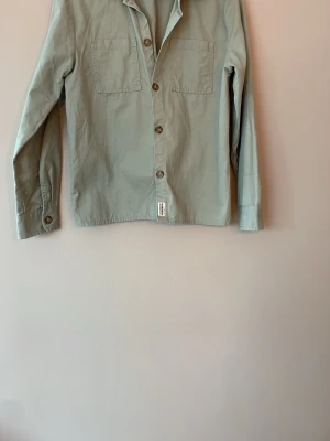 Ljusgrön overshirt med fickor - Stilren ljusgrön overshirt med två bröstfickor och knappar framtill. Skjortan har klassisk krage och långa ärmar med knapp vid ärmslut. Tillverkad i ett mjukt bomullstyg som känns bekvämt och passar perfekt till lager på lager.