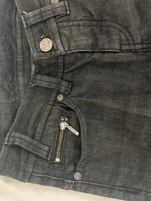 Svarta jeans från Diesel med dragkedjedetalj - Säljer ett par svarta jeans från Diesel med snygg dragkedjedetalj vid fickan och klassiska fem fickor. Jeansen har silverfärgade nitar och logga på bakfickan. Materialet är slitstark denim i bomull. Original pris 1300