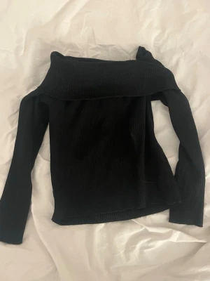 Svart off shoulder topp - Trendig svart off shoulder topp med långa ärmar och bred krage. Ribbad struktur i tyget ger en snygg och modern look. 