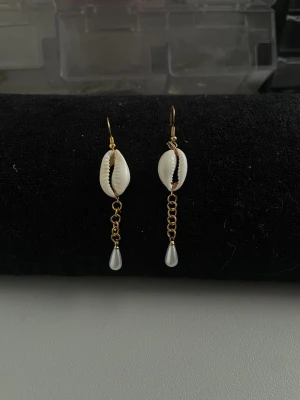 Viana earrings  - Unika örhängen med guldfärgad krok, vit snäcka och kedja som avslutas med en liten droppformad pärla. Perfekt för dig som gillar boho-vibbar och strandinspirerad stil. Säljs som par. Man kan även säga till mig så kan jag flytta pärlan högre upp💗