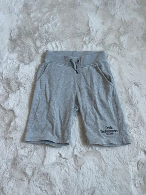 Grå shorts Peak Performance - Snygga grå shorts från Peak Performance med broderad logga på benet och praktisk snörning i midjan. Tillverkade i mjukt material som känns skönt mot huden. Perfekta för varma dagar eller chill hemma.