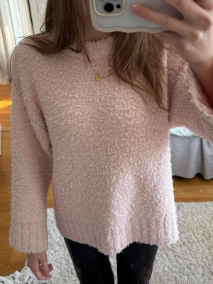 Ljusrosa fluffig stickad tröja - Mysig ljusrosa stickad tröja med fluffig textur och rund hals. Tröjan har långa ärmar och oversize passform. Passar storlekar mellan s-L, perfekt för att hålla värmen. Materialet känns mjukt och bekvämt mot huden. Enkel och stilren design utan synligt märke.