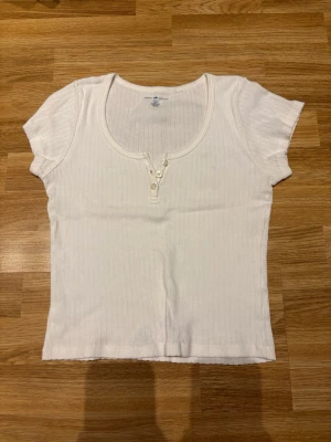 Vit ribbad topp med knappar - Snygg vit topp med korta ärmar och rundringning samt tre knappar fram. Från brandy Melville