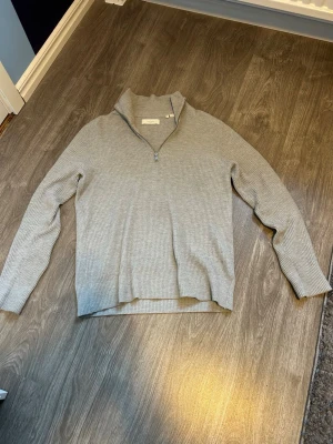 Grå ribbad half zip-tröja Jack & Jones - Säljer en stilren grå ribbad stickad tröja från Jack & Jones. Tröjan har en halv dragkedja vid halsen och lång ärm. Perfekt till chill vardagsstil och enkel att matcha med jeans eller chinos.