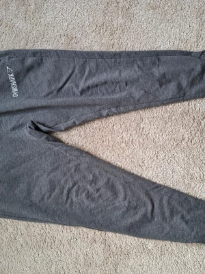 Grå mjukisbyxor från Gymshark - Säljer ett par grå mjukisbyxor från Gymshark med smal passform och resår i midjan. Byxorna har diskret Gymshark-logga på höften och är tillverkade i mjukt och stretchigt material som passar perfekt för chill eller träning.