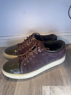 Vinröda lanvin - Snygga vinröda sneakers med ovandel i mocka och glansig, mörkgrön lackad tå. Skorna har vita sulor och metallfärgade öljetter. Klassisk låg modell med snörning och kontrasterande materialval som sticker ut.