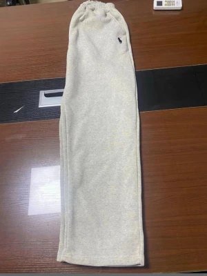 Grå mjukisbyxor från Polo Ralph Lauren - Snygga ljusgrå mjukisbyxor från Polo Ralph Lauren med klassisk broderad logga i marinblått på benet. Byxorna har resår i midjan och är gjorda i mjukt bomullsmaterial för maximal komfort. Perfekta för chill dagar eller när du vill ha en avslappnad stil.