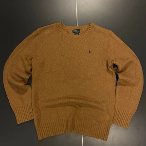 Brun stickad tröja från Polo Ralph Lauren - Snygg brun stickad tröja från Polo Ralph Lauren med rund halsringning och ribbade muddar. Tröjan har mörkbruna mockadetaljer på armbågarna och den klassiska lilla loggan broderad på bröstet. Perfekt för dig som gillar stilrena och tidlösa plagg. Storlek 18-20 vilket motsvarar ungefär en vanlig S i man.