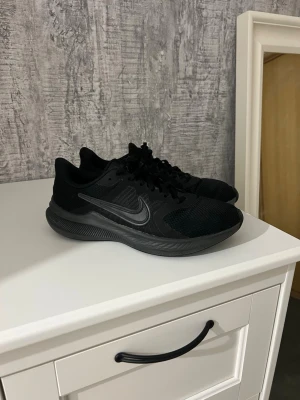 Nike Downshifter 11 - Säljer ett par Nike Downshifter 11 i färgen "Triple Black". En riktigt lätt och skön sko som funkar lika bra för löprundan som till vardags eller på gymmet. Storlek 40 små defekter se bild inga hål 