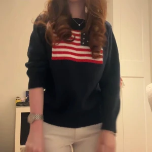 Mörkblå stickad tröja med USA-flagga - Säljer en mörkblå stickad tröja med en stor amerikansk flagga i rött, vitt och blått på bröstet. Tröjan har rund halsringning och långa ärmar. Perfekt för dig som vill ha en klassisk och cool look.