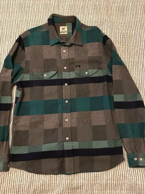 Lee skjorta - Säljer en rutig skjorta från Lee i gröna, gråa och svarta rutor. Skjortan har lång ärm, två bröstfickor med knappar och klassisk krage. Jag är 174 och den sitter lite baggy på mig.
