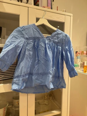 Blå luftig blus med trekvartsärm - Söt blå blus i bomull med v-ringning och trekvartsärmar. Blusen har dekorativa sömmar och lätt rynkade detaljer som ger en avslappnad och trendig look. Perfekt att matcha med jeans eller kjol för en fräsch stil. Just nu skrinklig men det går lätt att fixa