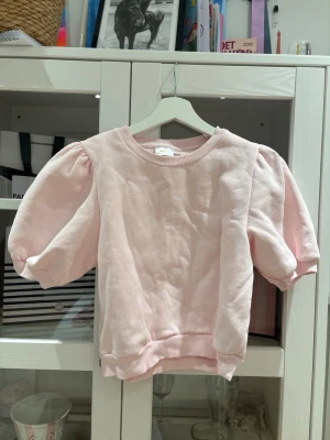 Ljusrosa puffärm topp - Supersöt ljusrosa topp med puffärmar och ribbade muddar. Toppen har en relaxed fit och är tillverkad i mjukt bomullsmaterial. Perfekt för dig som vill ha en enkel men trendig look.