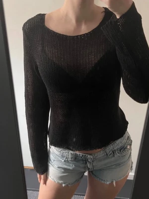 Svart transparent stickad tröja - Säljer en svart, långärmad stickad tröja med transparent och luftig struktur. Tröjan har en rund halsringning och är något lös i modellen, perfekt för lager på lager. Materialet känns mjukt och följsamt, vilket gör den skön att bära.