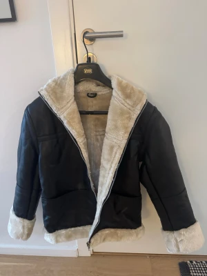 Svart Sherling jacka med beige foder - Snygg svart sherlingjacka (äkta skinn) med mjukt beige foder och detaljer vid krage, ärmslut och nederkant. Jackan har dragkedja framtill och två fickor. Aldrig använd köpt på Etsy, saknar prislapp dock. Storlek M enligt storleks tabell (se bild för storlekstabell) men jag uppfattar den som liten snarare en small eller 36.