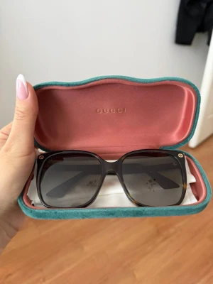 Gucci Solglasögon med vit båge och svart lins - Snygga solglasögon med vit, rundad båge och mörka svarta linser. Klassisk och stilren design som passar perfekt till sommarens outfits. Bågen är tillverkad i syntetmaterial och har en modern look.