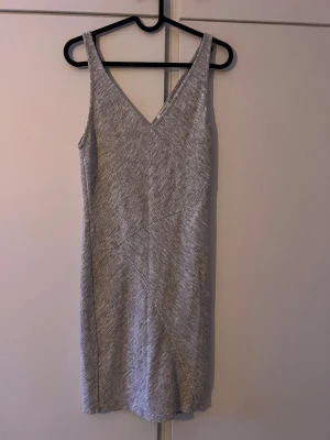 Grå ärmlös klänning från Bershka - Snygg grå kortklänning från Bershka med v-ringad hals och ärmlös design. Klänningen har diskreta diagonala sömmar som ger en cool struktur och är gjord i mjuk bomullsmix. Perfekt för dig som gillar enkel men stilren look.