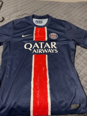 PSG matchtröja blå Nike - Äkta!!!!!Snygg blå Paris Saint-Germain matchtröja från Nike med röd och vit rand i mitten. PSG-logga på bröstet och Qatar Airways tryckt på framsidan. Tillverkad i lätt och ventilerande material, perfekt för fotbollsträning eller match.