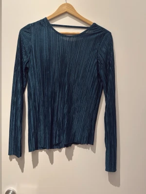  ribbad långärmad topp - Snygg långärmad topp med ribbad struktur och djup v-ringning i ryggen. Materialet har en lätt glansig finish som ger en cool look. Perfekt att styla med både jeans och kjol. Den är mer grön i verkligheten än vad som går att få fram på bild 