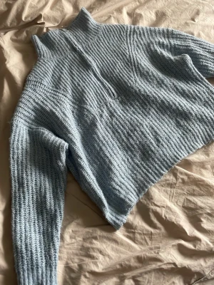 Ljusblå stickad halvzip tröja - Mysig ljusblå stickad tröja med halv dragkedja och hög krage. Tröjan har en avslappnad passform, ribbstickade detaljer och långa ärmar. Perfekt för lager på lager och chill dagar.