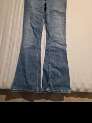 Blå utsvängda jeans bootcut - Säljer ett par klassiska blå jeans med utsvängda ben, bootcut-modell. Jeansen har låg midja och femficksdesign. Tillverkade i denim med snygg tvättad look. Perfekta för dig som gillar retrostil och vill ha ett par bekväma jeans med lite extra attityd.