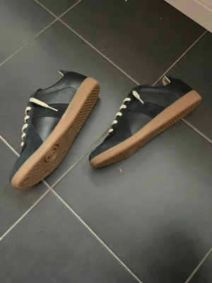 Maison Margiela Gats - Hej! Säljer mina svarta Maison margiela gats. Storlek 43. Köpta i samband med mina vita från NK. Inte fått någon användning av dem och har inte kunnat lösa en retur. Har all kvittering. Skriv om ni har frågor. Uppskattar snabb affär. Söker 2999 men skicka gärna bud. 