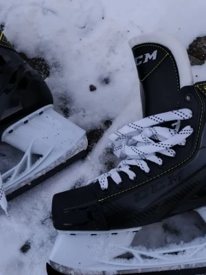 Svarta CCM hockeyskridskor - Säljer ett par svarta hockeyskridskor från CCM med vita snören och detaljer i gult. Skridskorna har robust konstruktion och är perfekta för isen. Klassisk design med vit sula och svart ovandel. Pris går super bra att diskutera! 