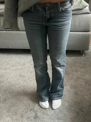 Bootcut jeans med detaljerade fickor - Snygga blå bootcut jeans med ljusa slitningar och dekorativa sömmar på bakfickorna. Klassisk femficksmodell med låg midja och dragkedja. Perfekta för en avslappnad och trendig look.