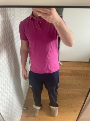 Rosa pikétröja från Ralph Lauren - Säljer en klassisk rosa pikétröja från Ralph Lauren med korta ärmar och krage. Tröjan har knappar vid halsen och den ikoniska loggan broderad på bröstet. Perfekt för en avslappnad men ändå stilren look.