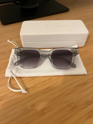 Gråa solglasögon från CHIMI - Snygga solglasögon från CHIMI i transparent grå färg. De har en modern, kantig form och levereras med originalfodral och tygpåse. 