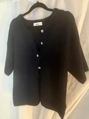 Stickad trekvarts - Mysig mörk marinblå/svart kofta från Gina Tricot med trekvarts ärmar och rund halsringning. Koftan har en lös passform och stängs med vita knappar framtill. Materialet är fluffigt och mjukt. Perfekt för lager på lager och en chill look. Helt oanvänd. Nypris: 329:-