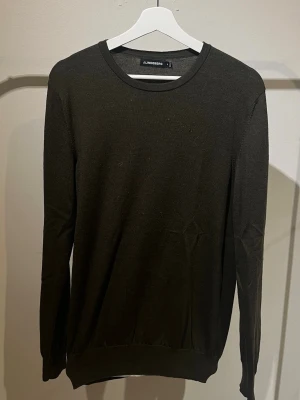  Stickad tröja från J.Lindeberg - Snygg mörkgrön långärmad tröja från J.Lindeberg med rund halsringning. Tröjan har diskret logga på bröstet och är tillverkad i ett tunt, stickat material som passar perfekt till lager-på-lager-stil.