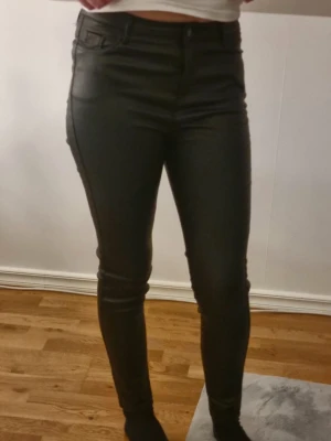 Svarta coated skinny skinnbyxor  - Snygga svarta skinny skinnbyxor med coated finish som ger en läderliknande look. Hög midja, klassisk femficksmodell och åtsittande passform. Perfekta för dig som vill ha en trendig och edgy stil.