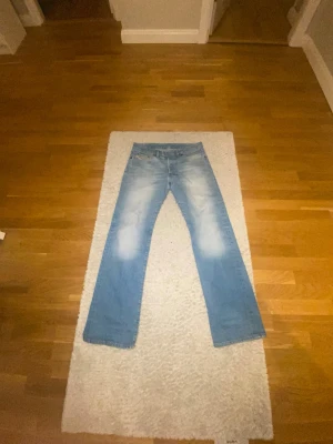 Blå bootcut jeans från Diesel - Säljer ett par ljusblå bootcut jeans från Diesel med klassisk femficksdesign och snygga slitningar framtill. Jeansen har en relaxed passform och är perfekta för en avslappnad stil. Diesel-logga på myntfickan ger extra detalj.