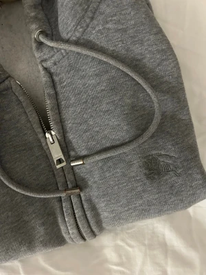 Burburry kofta  - Tja. Säljer en Burburry kofta i grå färg. Storlek L Men passar bättre som M/ Modellen på bilden är 1.80. / lite färg som kommit på högra ärmen(syns knappt), annars i väldigt bra skick. Självklar äkta. Kvitto kanske tillkommer/ ligger i mailen. DMa💥